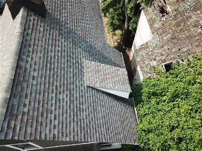 Drone view looking down on a shingle roof slope with an ivy-covered brick building to the right.