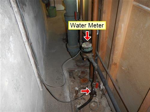 An old cellar passage with a water meter and generations of plumbing along the wall.