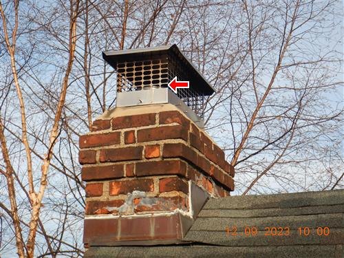 Brick chimney with a metal mesh cap, red arrow on the screen, broken brick at the roofline