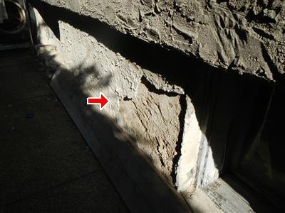 Cement parging broken away from the base of a wall, red arrow at the damage