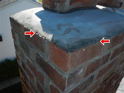 Brick chimney corner with a cement-washed top, two red arrows at chipped edges