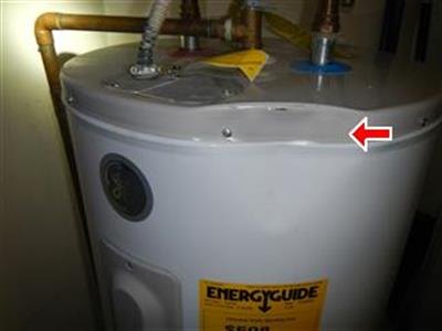 Top of an electric water heater with copper piping, red arrow at the tank rim