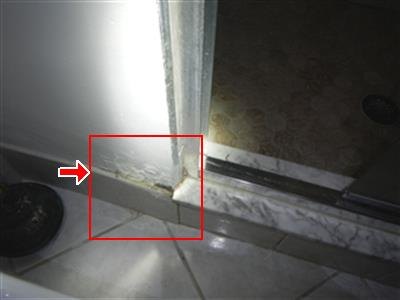 Corner of a shower door frame at a marble curb, red box and arrow at a stained joint