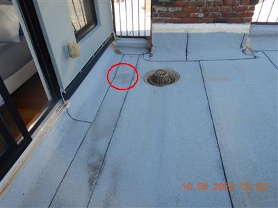 Silver-coated flat roof with metal drain strainer and a red circle marking a spot near a seam