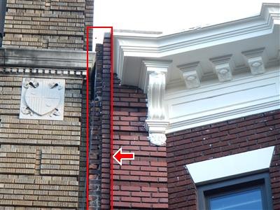 An ornamented facade with a vertical crack boxed in red along a brick pier beside the cornice.