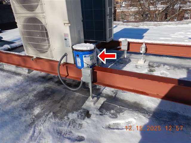 Snow-covered flat roof with two condenser units on steel rails and red arrow at a bucket covering equipment