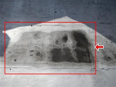 Flat roof membrane with a dark stained rectangular area outlined in red with an arrow