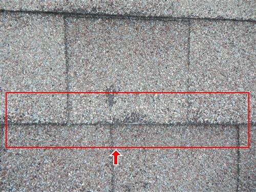 Close-up of asphalt shingles with a red box and arrow marking a damaged strip