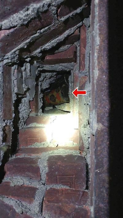 Looking down into a brick fireplace flue with a red arrow pointing at bottles and beer cans lodged inside.