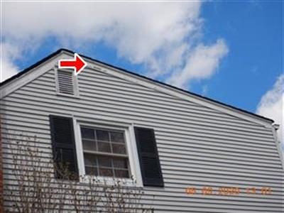 Gable end of a grey vinyl-sided house with a red arrow pointing at the upper fascia board.