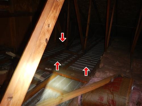 Attic with ceiling joists where three red arrows mark bays with no insulation and bare lath showing.