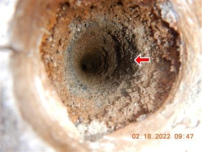 Close-up looking down a short rusted fill pipe into a dark hole, red arrow pointing into the opening.