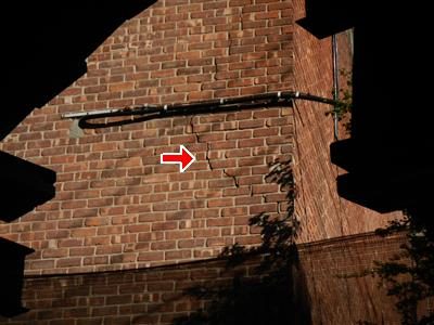 Brick corner of a building at night with a vertical crack running through the mortar joints, red arrow.
