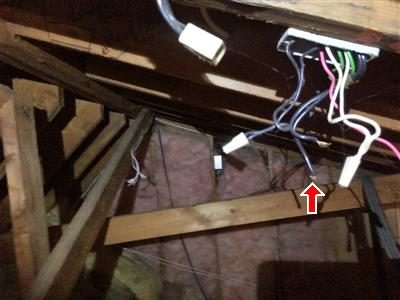 Attic rafters with loose wiring and an exposed wire connection hanging near a junction box, marked by a red arrow.