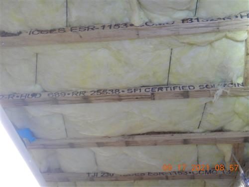 Basement ceiling showing wood I-joists with stamped lumber markings and yellow fibreglass insulation between them.