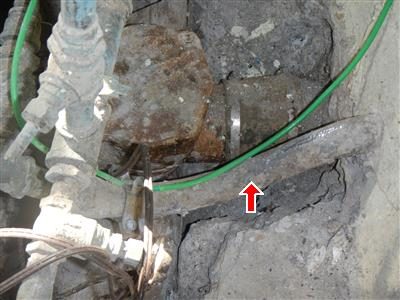 Old water service entry with a corroded meter and valve where the pipe enters through the foundation, marked by a red arrow.