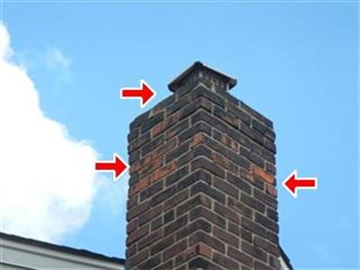 Brick chimney against a blue sky with red arrows pointing at peeling brick faces near the top.