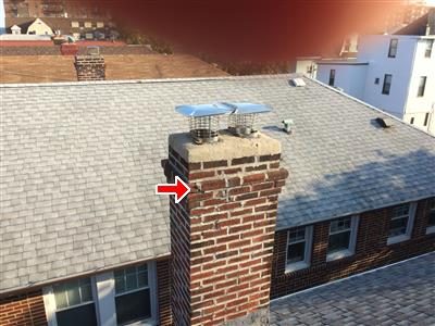 Brick chimney rising above a grey shingle roof with two metal caps, red arrow at the brickwork near the top.