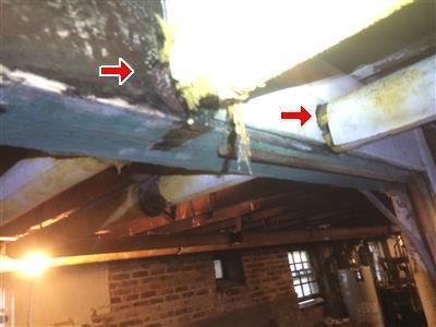 Insulated steam pipes passing through a wooden main beam in a basement, red arrows at the beam.