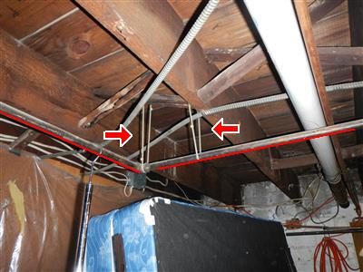 Basement ceiling joists with a black gas pipe outlined in red and two red arrows pointing at plastic ties holding it.