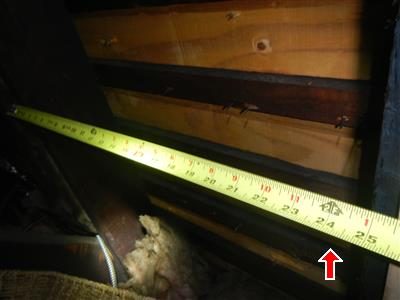 Tape measure stretched between attic rafters reading about 24 inches, marked by a red arrow.