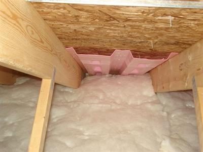 Attic rafter bay with white insulation and a pink plastic baffle against the roof sheathing.
