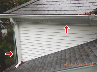 Roof-level view of white siding and dentil trim with red arrows marking exposed tubing along the soffit.