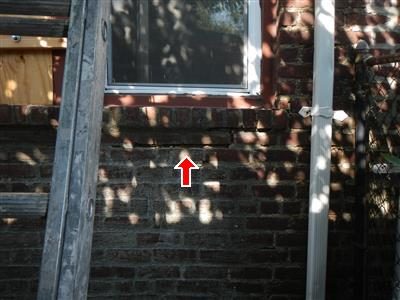 Brick wall below a window with a white leader pipe to the right, red arrow pointing up at open mortar joints.