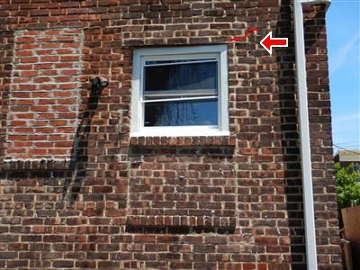 Brick wall around a rear window with a red arrow and short red line marking a step crack above the lintel.