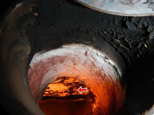 View into a boiler combustion chamber glowing orange with heavy scale deposits, red arrow on the heat exchanger.