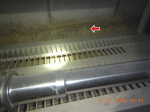 Concrete block basement wall above a baseboard heater with a dark stain line and a red arrow pointing to it.