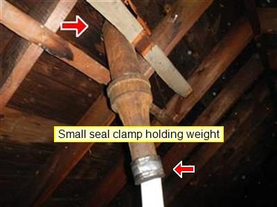 Old cast iron vent pipe at a basement ceiling joined to new white PVC pipe, with two red arrows and a seal clamp label.