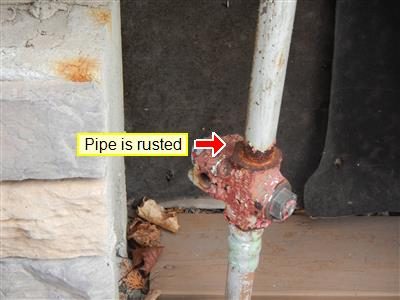 Heavily rusted red gas cock valve on a vertical pipe, labelled 