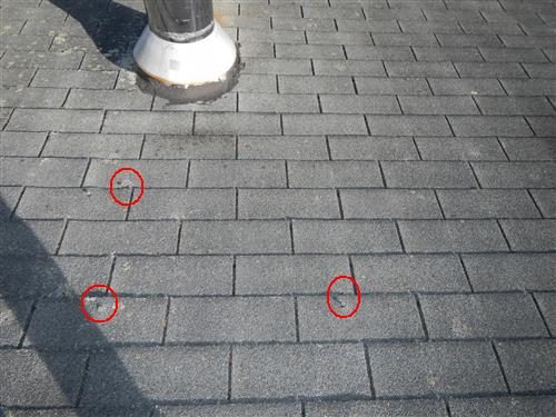 Grey asphalt shingles below a metal chimney with three red circles around nail pops.