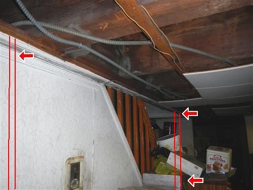 Basement ceiling with exposed joists and armoured cable above a stairwell, with red lines marking the header locations.