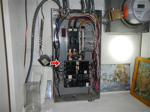 Open electrical panel with the cover removed, showing breakers and wiring, with a red arrow at a breaker on the left side of the stack.