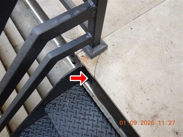 Black steel stair stringer and railing post on a rear deck, with a red arrow pointing at rust staining at the base.