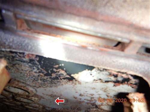 Close view inside a boiler showing rust-coloured, soot-covered cast iron sections, red arrow at the bottom.
