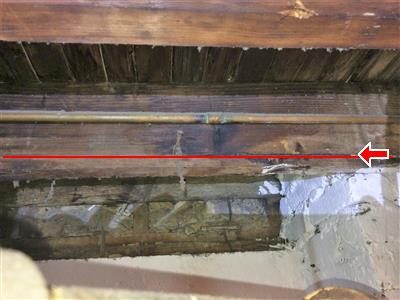 Basement floor joist with a copper pipe running alongside, red line and arrow marking a crack along the joist.