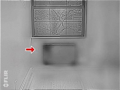 Greyscale FLIR infrared image of a bedroom window with a dark rectangular patch below it and a red arrow pointing at the patch.