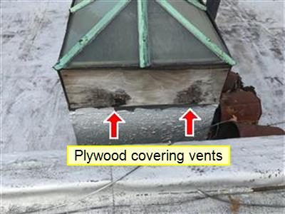 Copper-framed skylight on a flat roof with stained plywood over its vents, two red arrows and a label reading plywood covering vents.
