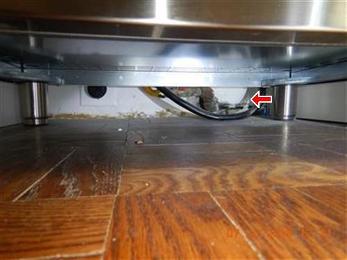 Gap behind a kitchen stove where a gas pipe passes through, with damaged wall and floor, marked by a red arrow.