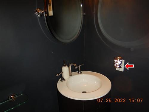 Dark bathroom with a round sink and mirror, red arrow at an outlet on the wall beside the mirror.