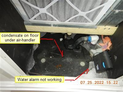 Floor under an air handler with condensate pooling beside a water alarm; report labels name the condensate and the alarm.