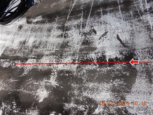 Flat roof surface with silver coating worn through and a red line along a seam, marked with a red arrow.