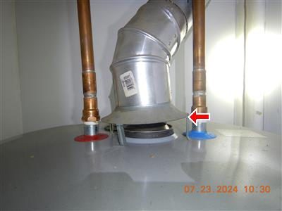 Top of a water heater with copper supply lines and a metal exhaust bonnet, red arrow at the base of the flue.