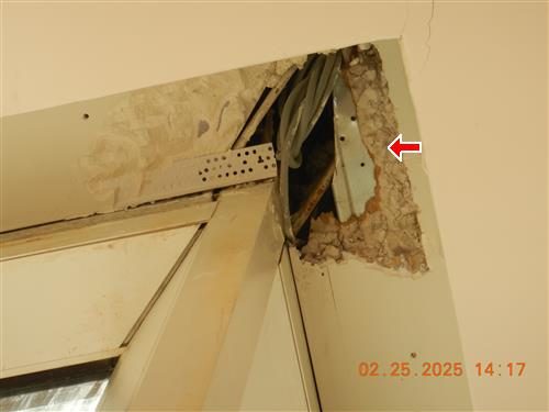 Corner of a ceiling above a door frame with plaster broken away exposing metal framing, red arrow at the damage.