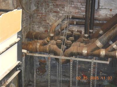 Large cast iron drain pipes with clean-out plugs and valves in a brick basement room.