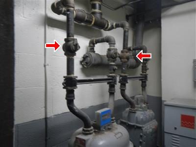 Black gas piping and two meters against a basement block wall, two red arrows pointing at valves.