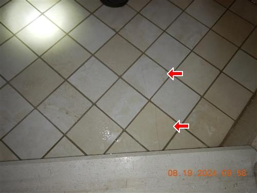 Beige ceramic tile shower floor with two red arrows pointing at hairline cracks across tiles.